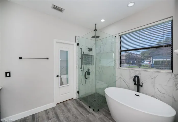 soaking tub and shower primary bathroom and door to walk in closet