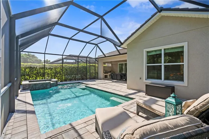Screened-in outdoor living space with a swimming pool and attached spa, surrounded by paver decking