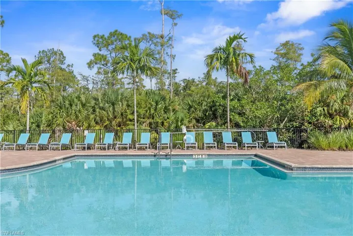 Expansive clubhouse swimming pool with a surrounding paver deck, featuring multiple lounge chairs and a metal safety fence