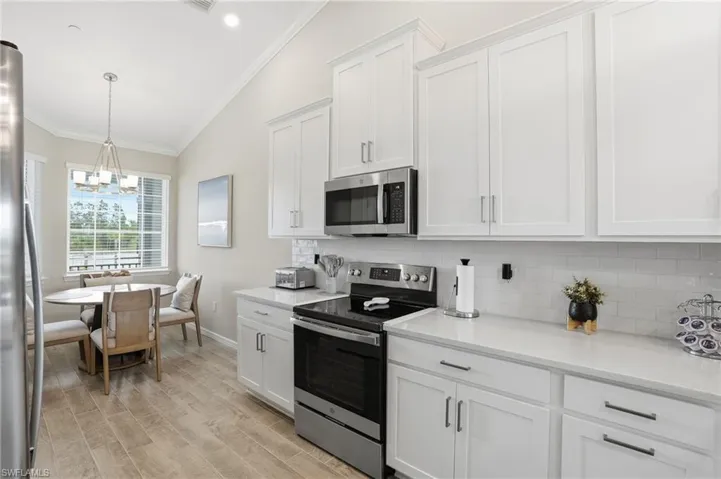 Kitchen featuring stainless steel appliances, crown molding, white cabinets, vaulted ceiling, and hanging light fixtures