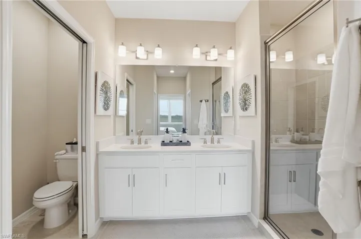 Bathroom featuring a shower stall, double vanity, and light tile patterned floors
