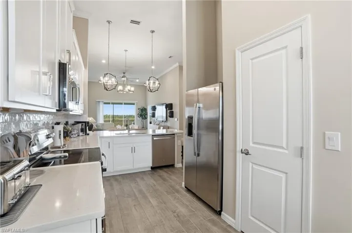 Kitchen featuring white cabinetry, stainless steel appliances, ornamental molding, decorative light fixtures, and light stone countertops