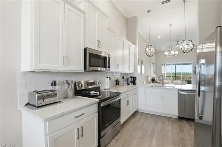 Kitchen featuring stainless steel appliances, white cabinetry, light stone countertops, tasteful backsplash, and crown molding