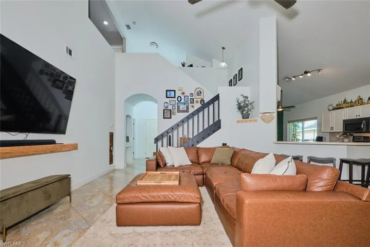 Living area with a ceiling fan, high vaulted ceiling, stairs, light marble finish flooring, and arched walkways
