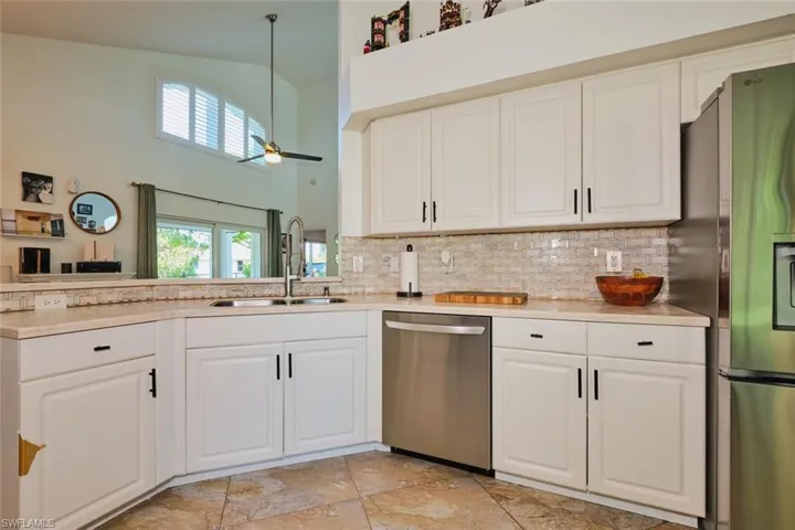 Kitchen featuring stainless steel appliances, a sink, backsplash, light countertops, and high vaulted ceiling