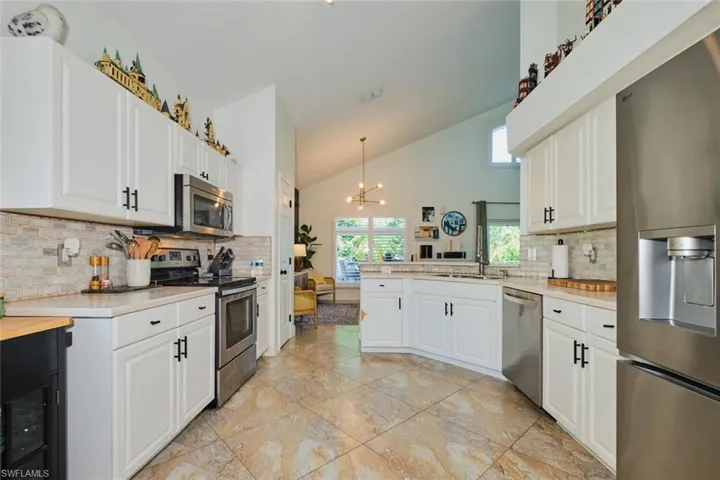 Kitchen with appliances with stainless steel finishes, light countertops, tasteful backsplash, white cabinetry, and high vaulted ceiling