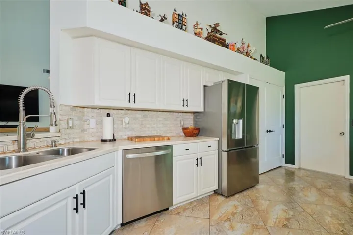 Kitchen with stainless steel appliances, a sink, decorative backsplash, light countertops, and a towering ceiling