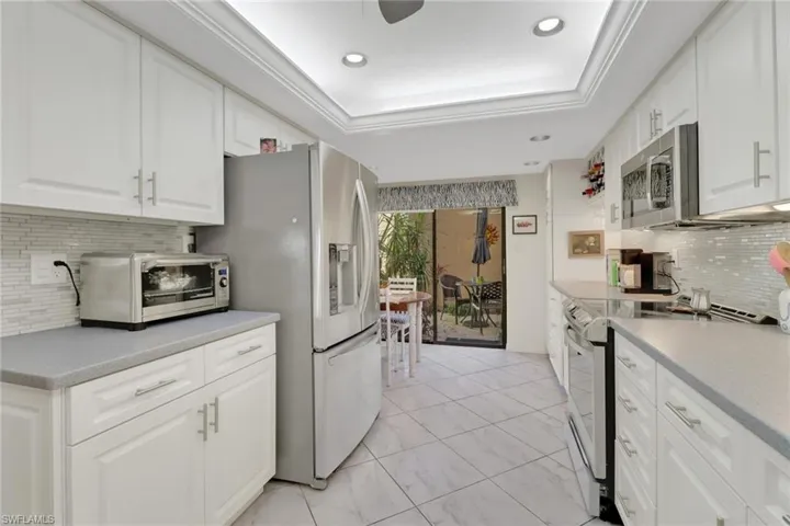 Kitchen featuring white cabinetry, stainless steel appliances, a raised ceiling, and backsplash