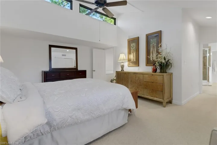 Bedroom with ceiling fan, light colored carpet, and high vaulted ceiling