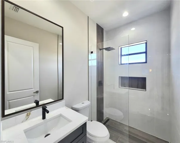 Bathroom featuring vanity, a tile shower, and toilet