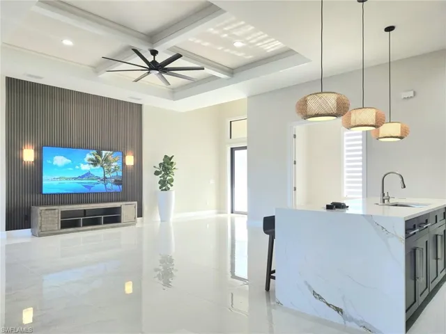 Kitchen with coffered ceiling, sink, hanging light fixtures, light stone countertops, and a kitchen island with sink
