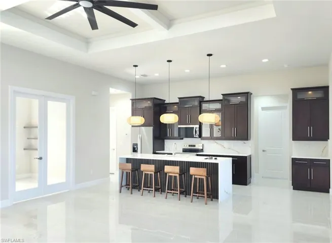 Kitchen with a kitchen island with sink, stainless steel appliances, dark brown cabinetry, decorative light fixtures, and french doors