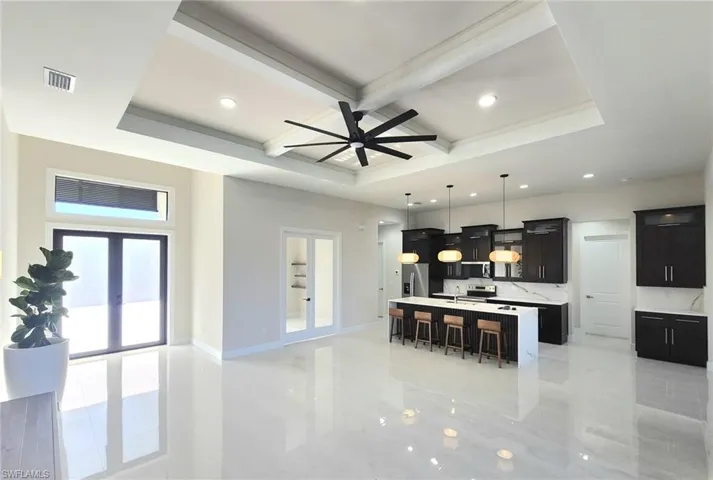 Kitchen with a breakfast bar, decorative light fixtures, an island with sink, coffered ceiling, and french doors