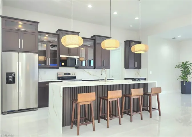 Kitchen with decorative light fixtures, sink, backsplash, stainless steel appliances, and a center island with sink