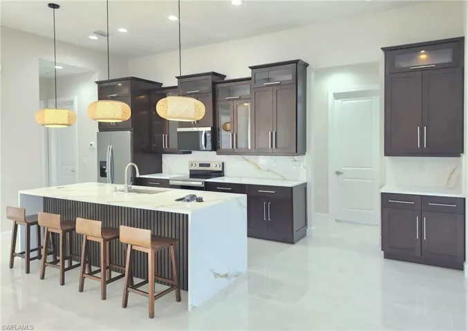 Kitchen with sink, decorative light fixtures, appliances with stainless steel finishes, and a center island with sink