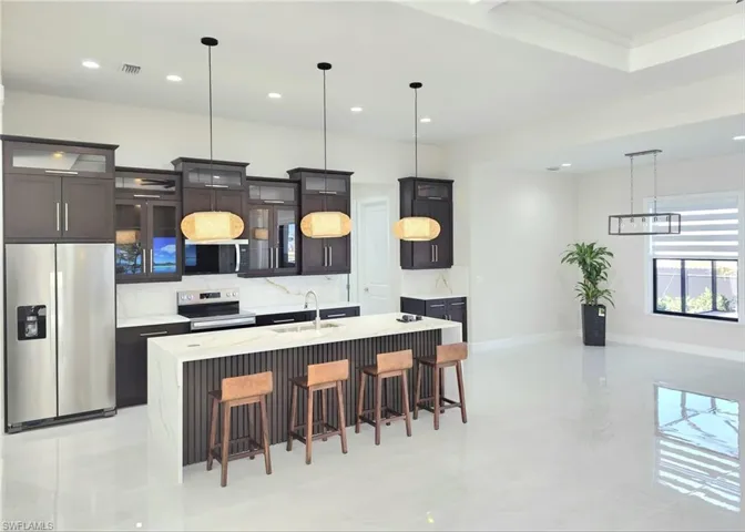 Kitchen with appliances with stainless steel finishes, sink, decorative light fixtures, and an island with sink