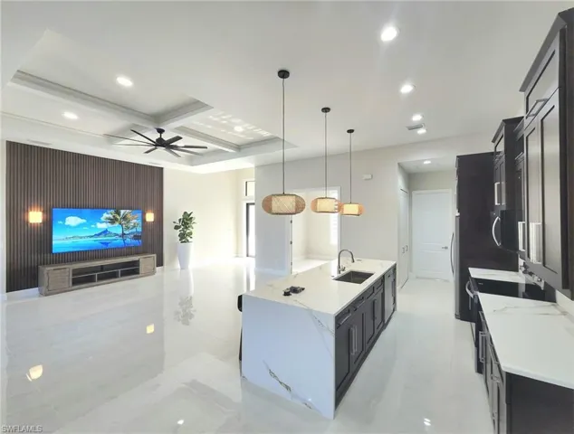 Kitchen with sink, a large island with sink, hanging light fixtures, coffered ceiling, and light stone countertops
