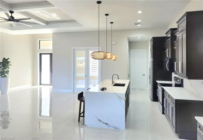 Kitchen with pendant lighting, sink, stainless steel appliances, light stone countertops, and a center island with sink