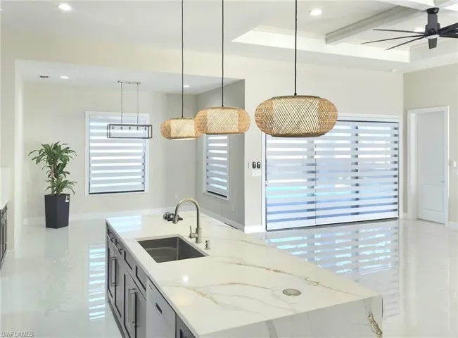 Kitchen featuring sink, light stone counters, hanging light fixtures, dishwasher, and an island with sink