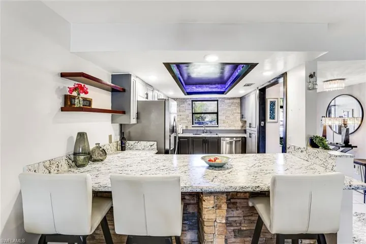 Kitchen with a kitchen breakfast bar, a tray ceiling, a peninsula, stainless steel appliances, and recessed lighting