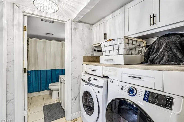 Laundry room featuring washer and clothes dryer, tile walls, light tile patterned flooring, and cabinet space