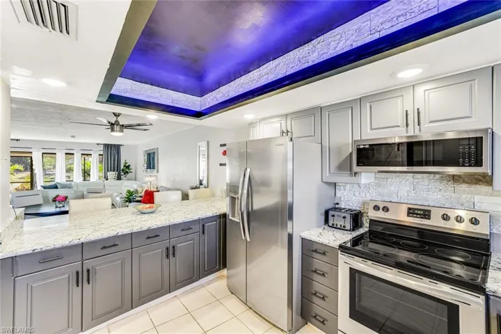 Kitchen with stainless steel appliances, gray cabinets, a raised ceiling, light stone counters, and open floor plan
