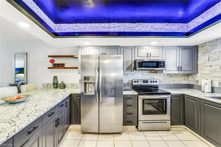 Kitchen with a raised ceiling, stainless steel appliances, recessed lighting, light stone countertops, and gray cabinets