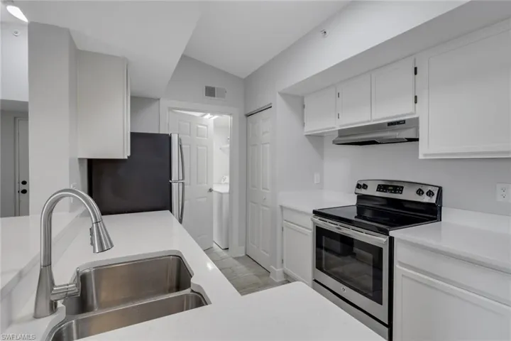 Kitchen with stainless steel appliances, white cabinetry, lofted ceiling, washer / clothes dryer, and light stone counters
