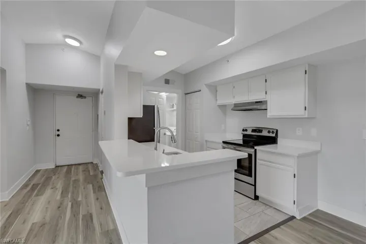 Kitchen with stainless steel appliances, white cabinetry, light wood-style flooring, a peninsula, and light stone counters