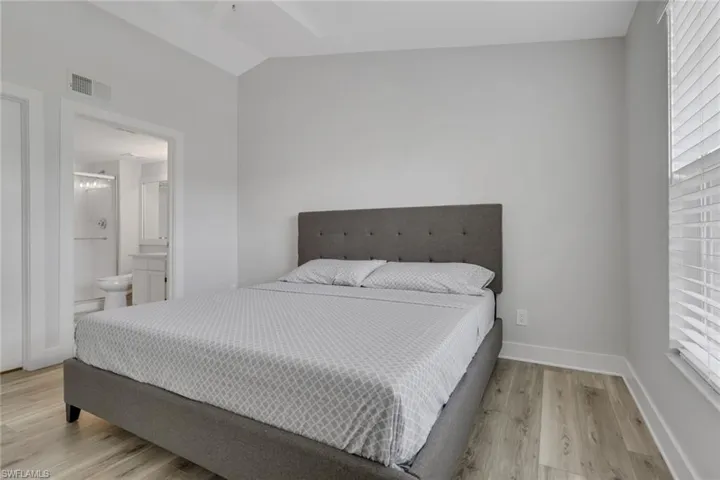 Primary bedroom featuring light wood-style flooring, vaulted ceiling, and ensuite bathroom