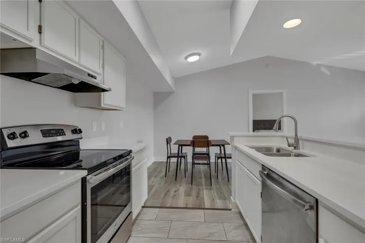 Kitchen with stainless steel appliances, white cabinets, lofted ceiling, and light stone countertops