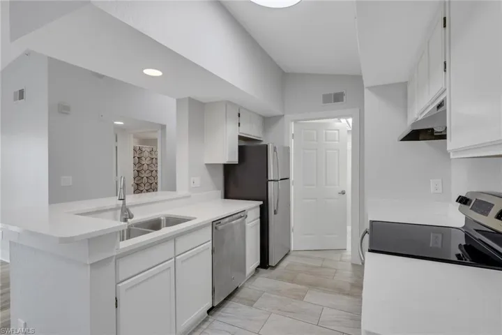 Kitchen featuring white cabinets, light countertops, stainless steel appliances, lofted ceiling, and a peninsula