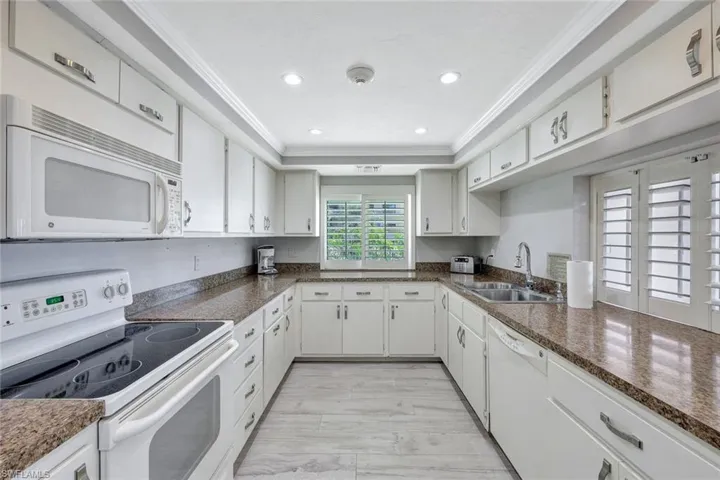 Kitchen featuring sink, white cabinets, white appliances, a raised ceiling, and ornamental molding