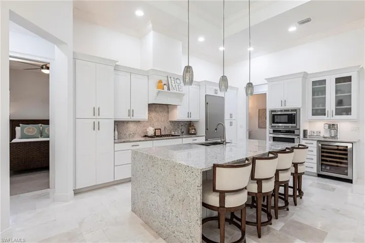 Kitchen with beverage cooler, a spacious island, ornamental molding, a sink, and built in appliances
