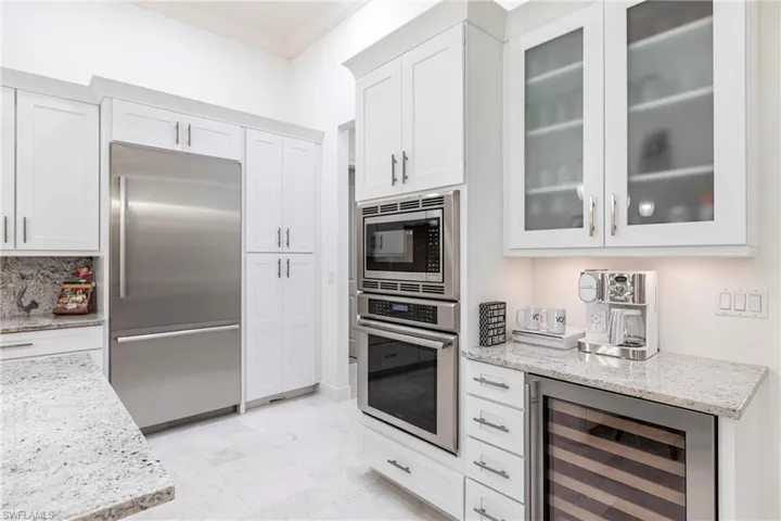 Kitchen with crown molding, beverage cooler, built in appliances, light stone counters, and white cabinets
