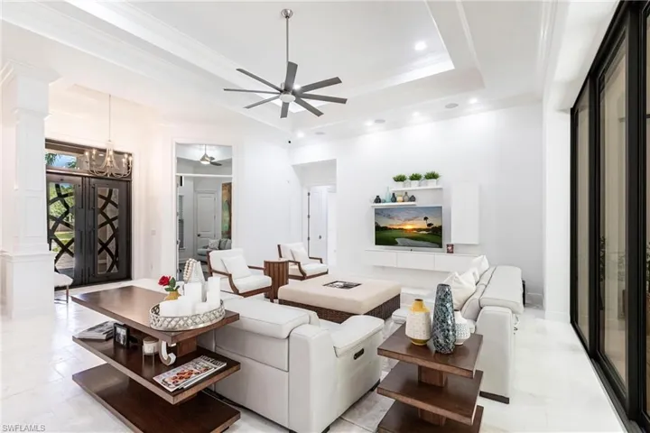 Living area with a tray ceiling, decorative columns, ornamental molding, recessed lighting, and ceiling fan with notable chandelier