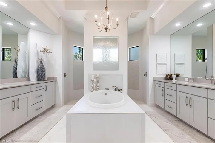 Full bathroom with an inviting chandelier, two vanities, a sink, a garden tub, and marble finish floor