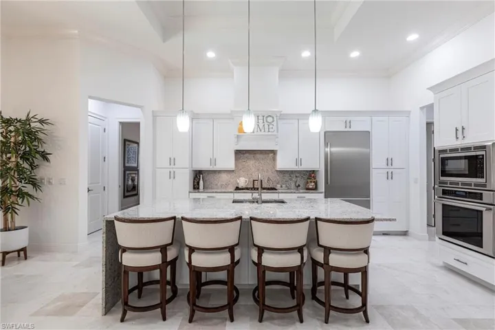 Kitchen with light stone countertops, built in appliances, an island with sink, ornamental molding, and decorative backsplash