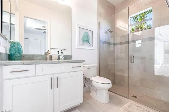 Full bathroom with tile patterned flooring, ceiling fan, toilet, a stall shower, and vanity