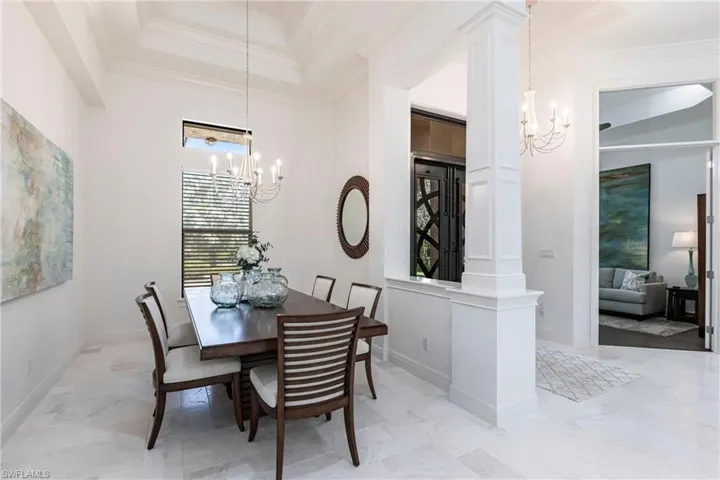 Dining space featuring a high ceiling, an inviting chandelier, crown molding, decorative columns, and baseboards