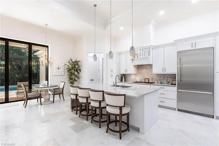 Kitchen with a center island with sink, a sink, appliances with stainless steel finishes, decorative backsplash, and light stone countertops