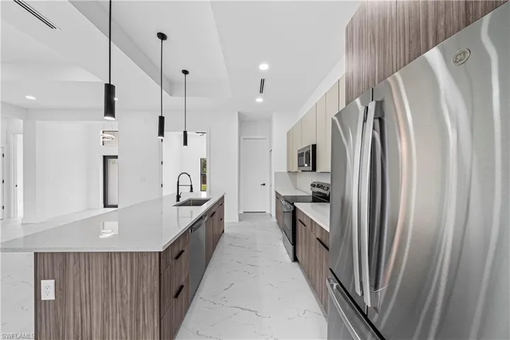 Kitchen with modern cabinets, stainless steel appliances, a large island with sink, light stone counters, and a tray ceiling