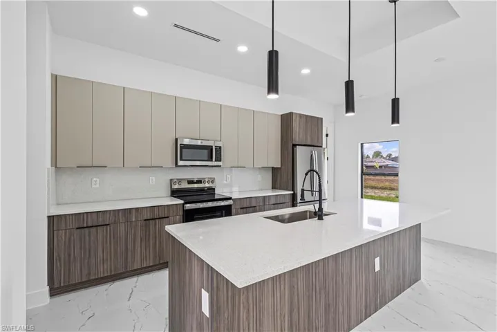 Kitchen featuring stainless steel appliances, light stone countertops, an island with sink, modern cabinets, and pendant lighting