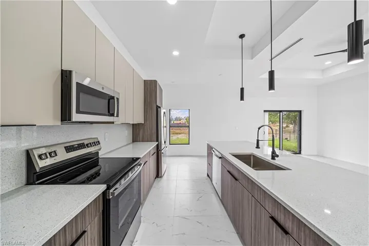 Kitchen featuring stainless steel appliances, a tray ceiling, light stone countertops, modern cabinets, and hanging light fixtures