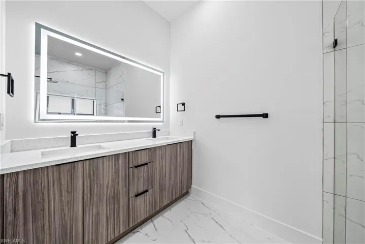 Bathroom featuring light marble finish floors, double vanity, and a marble finish shower