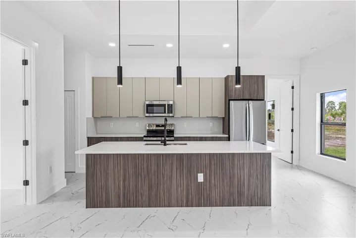 Kitchen with a kitchen island with sink, decorative light fixtures, stainless steel appliances, modern cabinets, and light stone counters