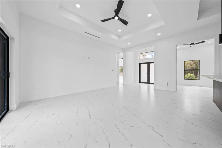 Unfurnished living room with a ceiling fan, recessed lighting, french doors, a tray ceiling, and light marble finish flooring