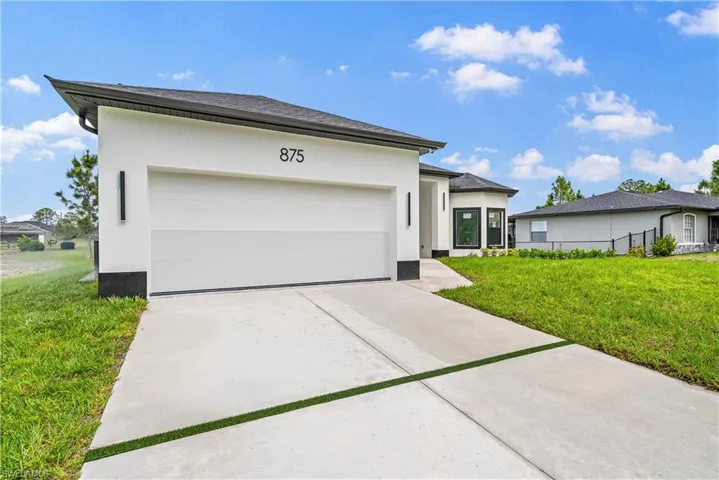 View of front of property featuring a front lawn, a garage, concrete driveway, and stucco siding