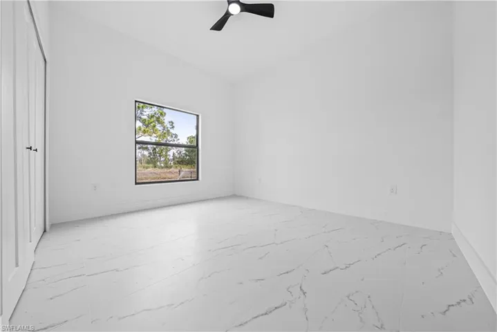 Spare room with lofted ceiling, light marble finish floors, and ceiling fan