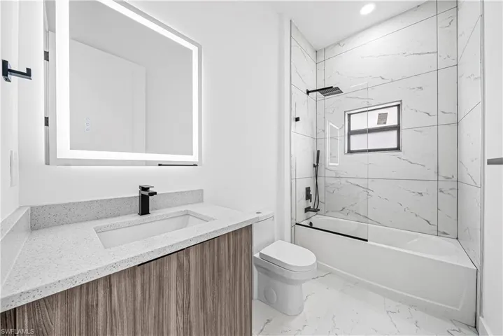 Bathroom featuring vanity, washtub / shower combination, light marble finish floors, and recessed lighting